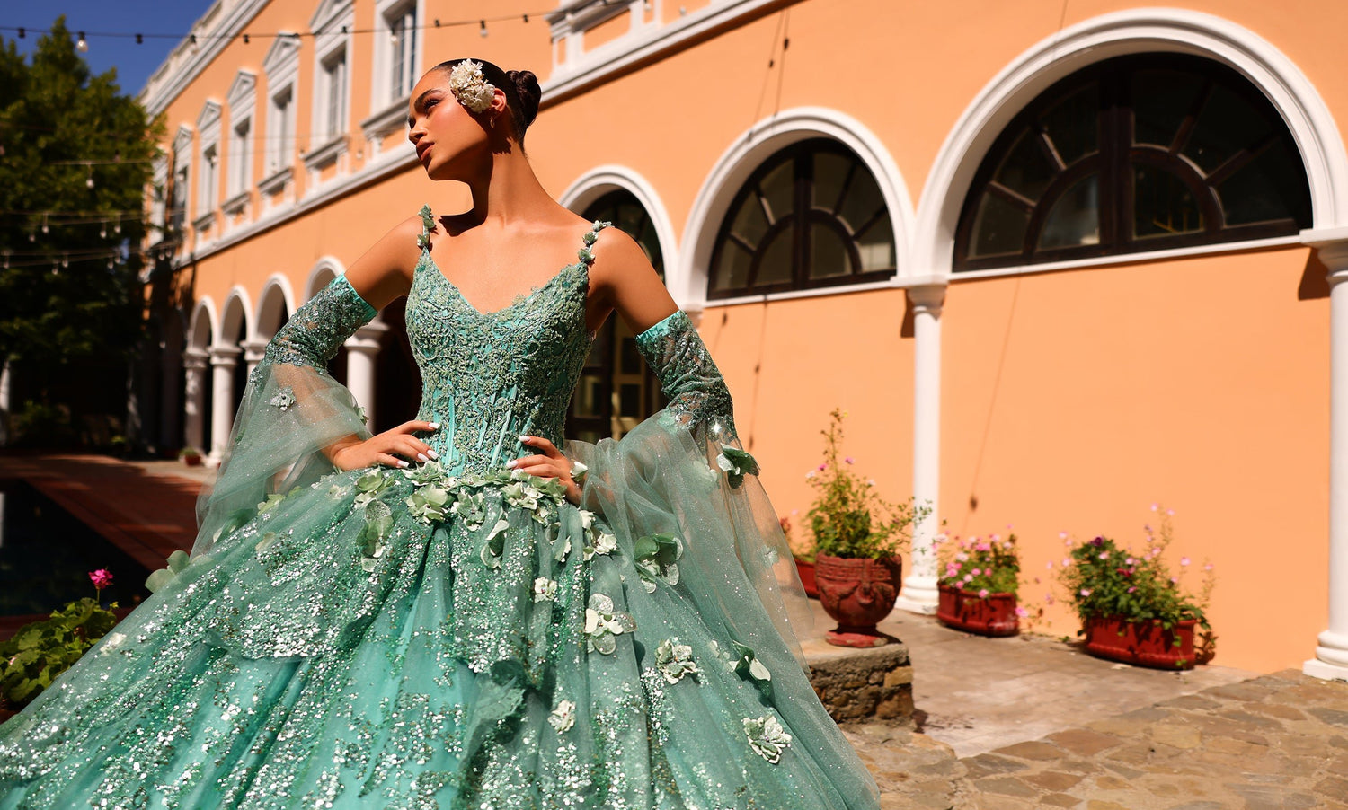 Model in a sage green ball gown with beaded corset bodice and sheer floral cape sleeves