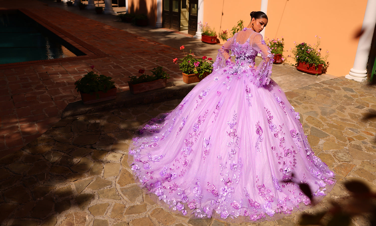Back view of a model beside a pool in a lilac ball gown covered in three-dimensional flowers