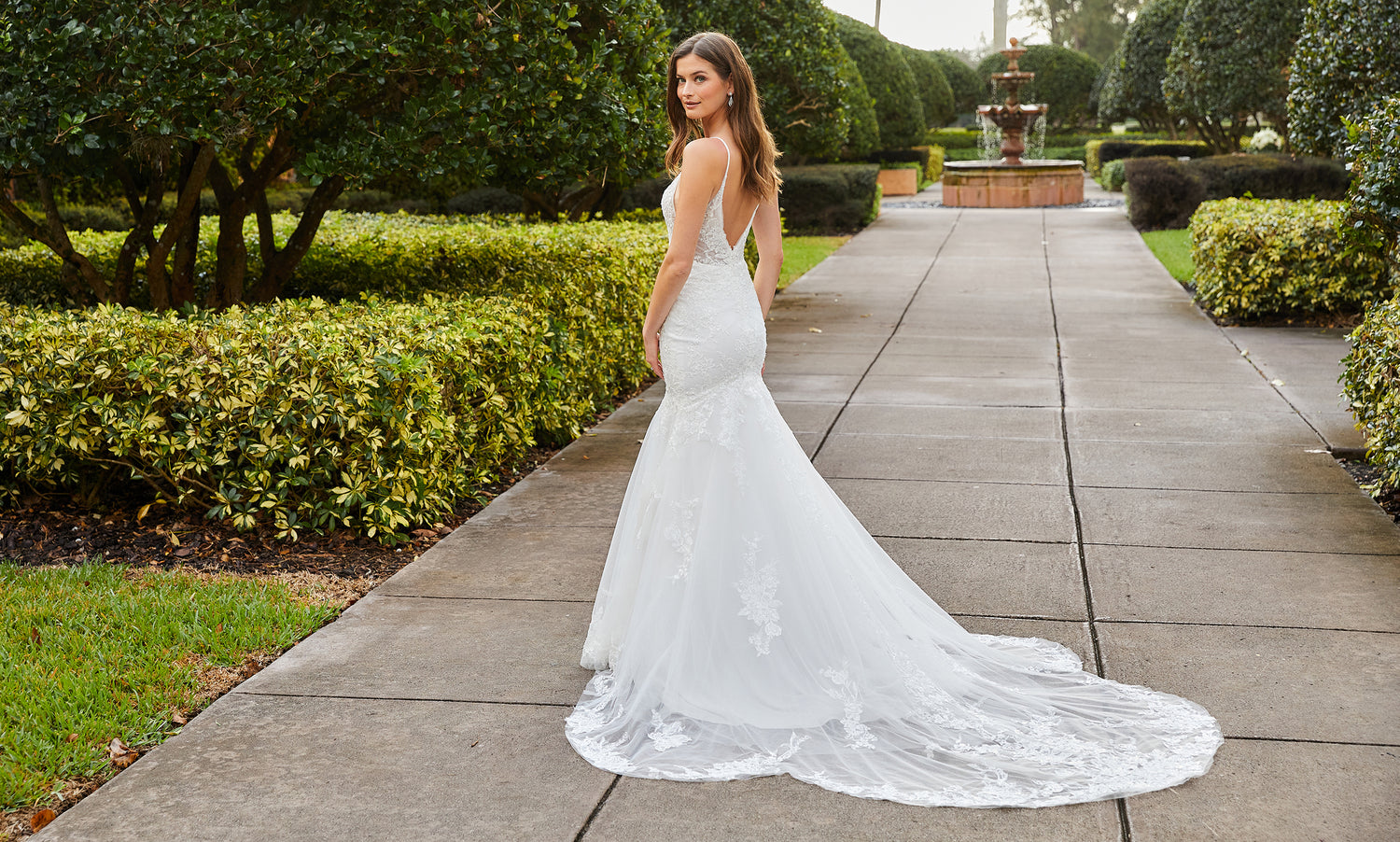 Brunette bride viewed from behind on a garden path, lace mermaid gown with a long trailing train