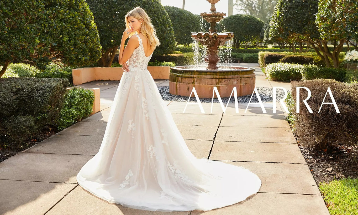 Bride seen from behind in a lace and tulle A-line gown with a long train by a garden fountain