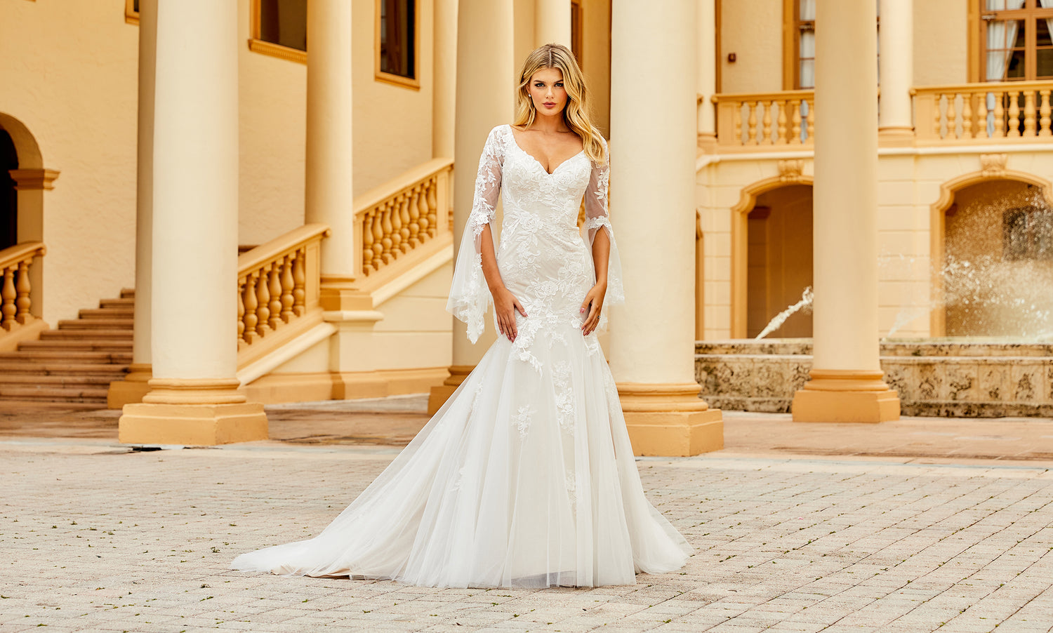Bride in a fitted ivory lace gown with sheer bell sleeves and flared tulle skirt outside a palazzo