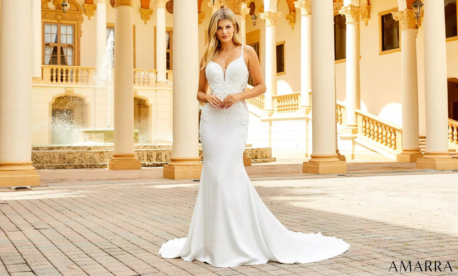 Bride in a fitted white gown with a lace bodice standing among courtyard columns and fountains