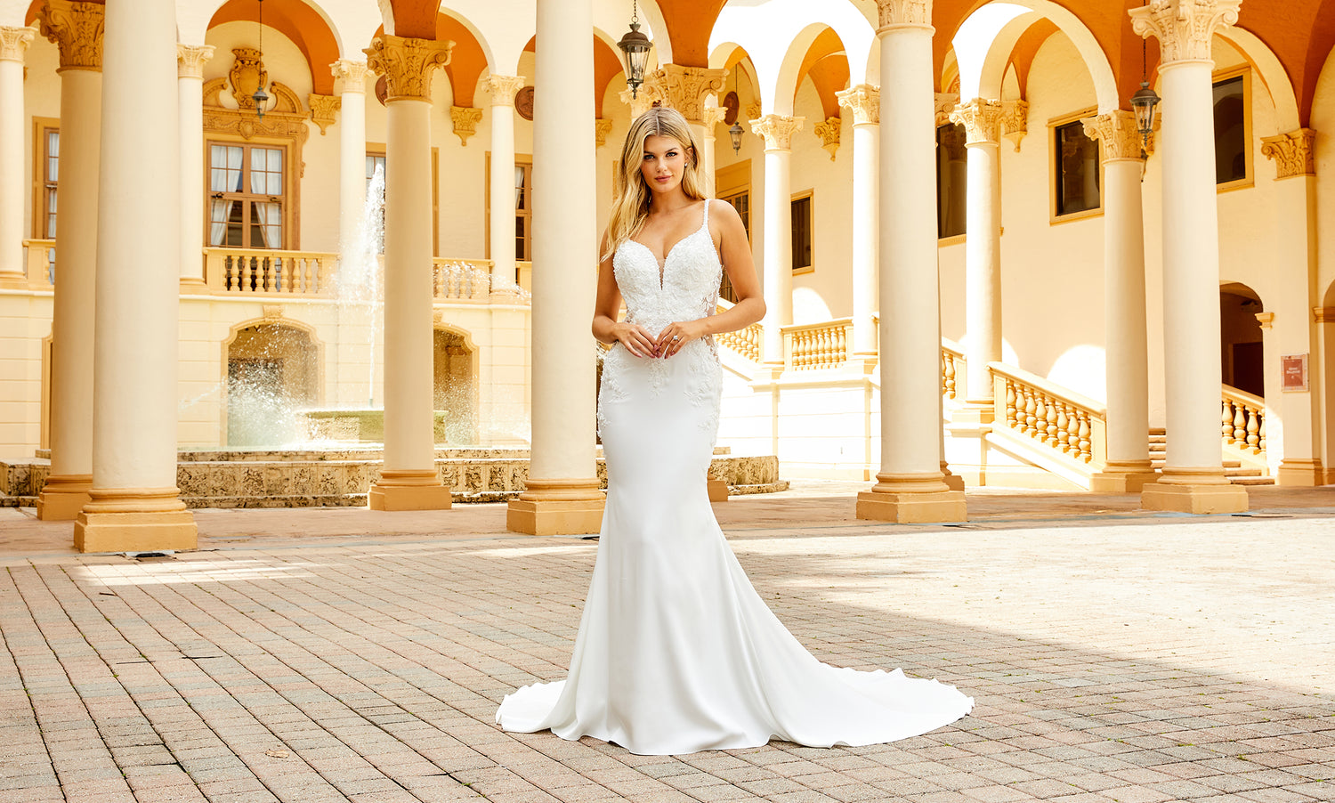Bride in a white crepe mermaid gown with beaded bodice standing in a golden palazzo courtyard