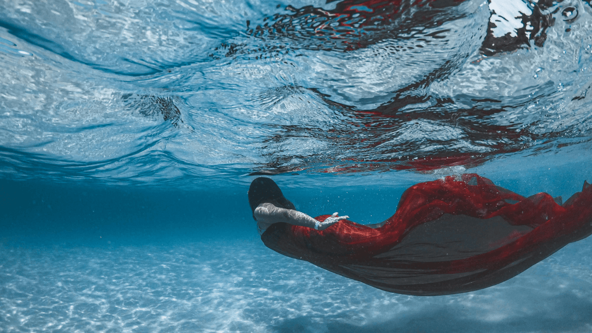 Underwater view of a woman in a flowing red gown floating just below the surface
