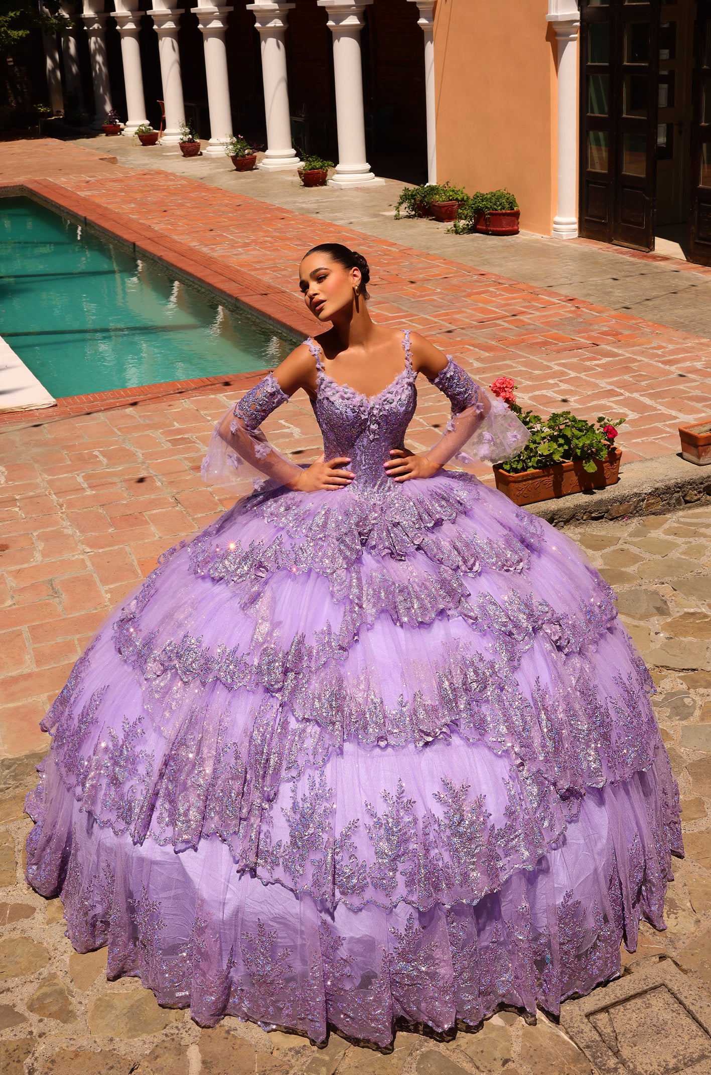 A dramatic lilac ball gown with sparkling embellishments poses by a pool in an elegant courtyard setting.