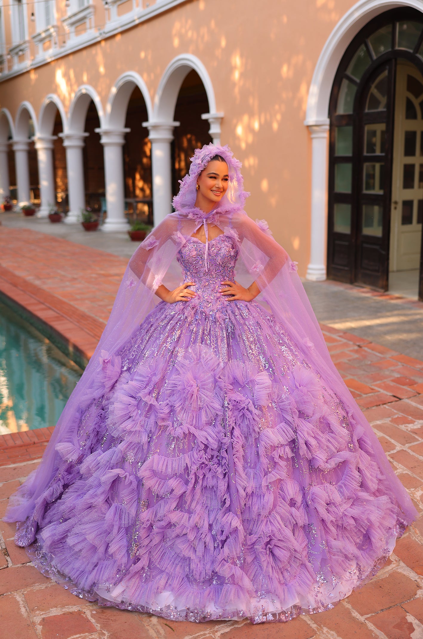 A woman wears a lavish purple ball gown with ruffles and a cape, posing by arched columns.