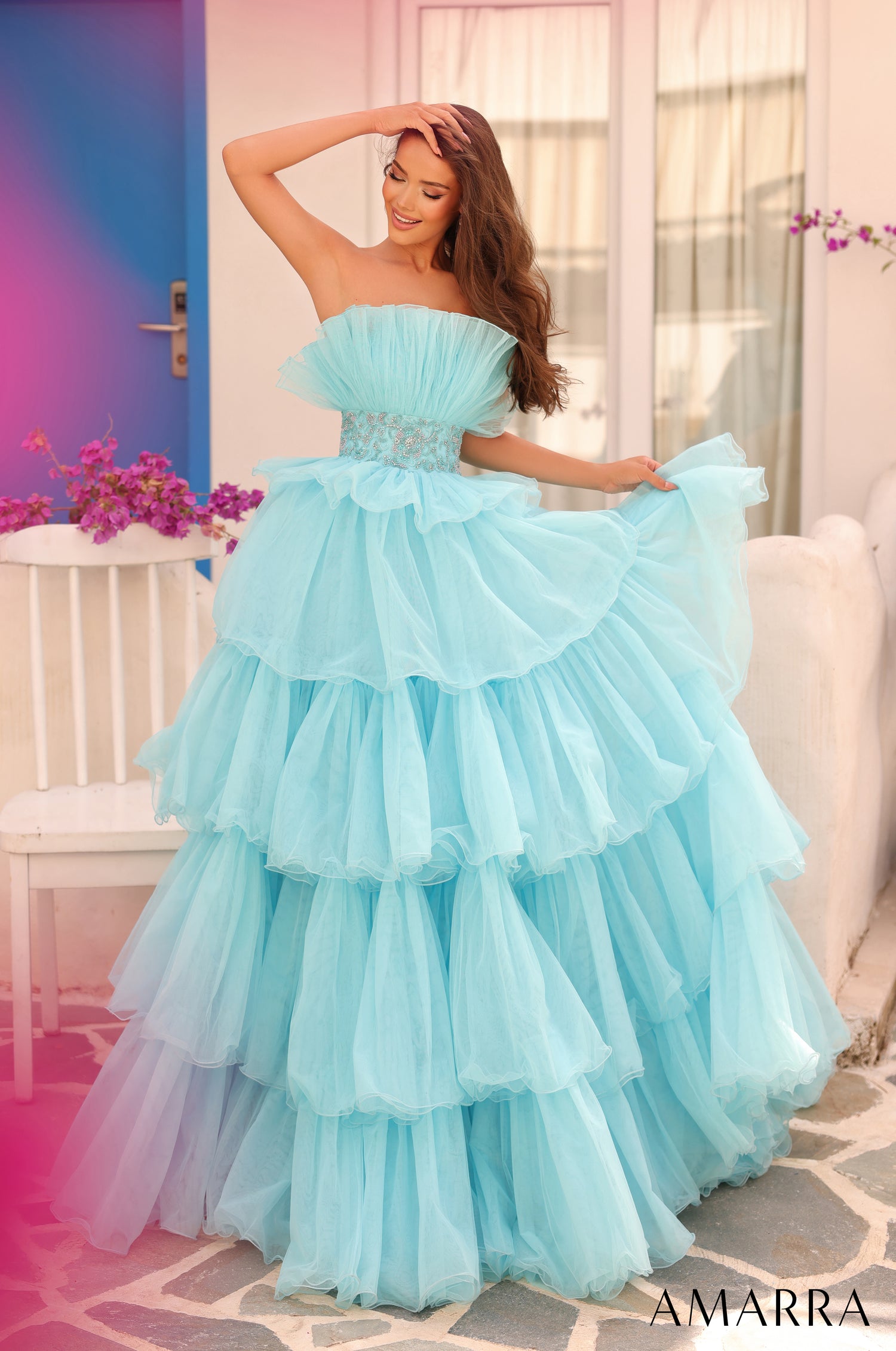 A woman wears a tiered aqua blue ruffled ballgown with a strapless bodice, posing elegantly.