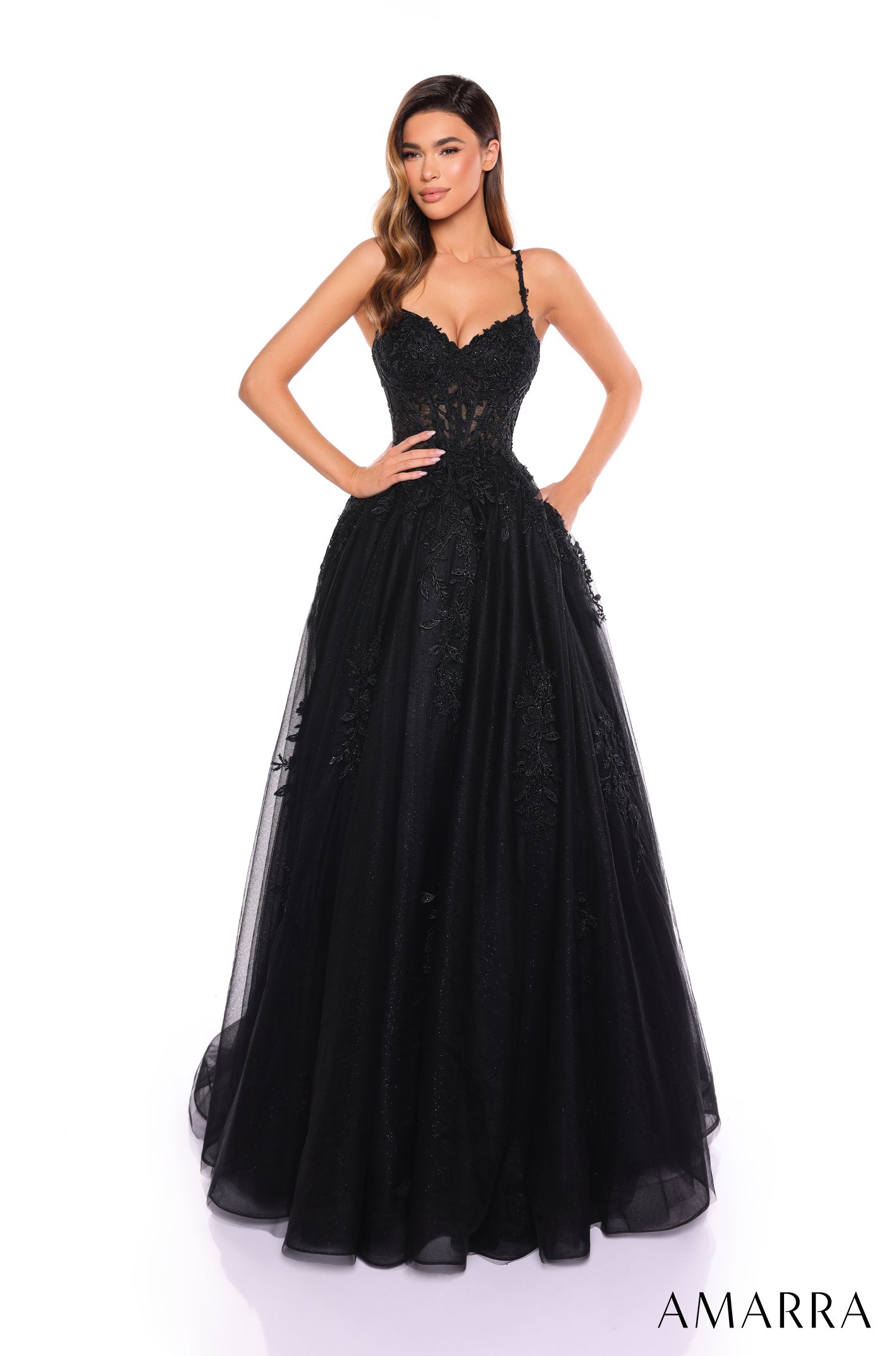 A woman wears a black lace corset ball gown with a full tulle skirt against a white background.