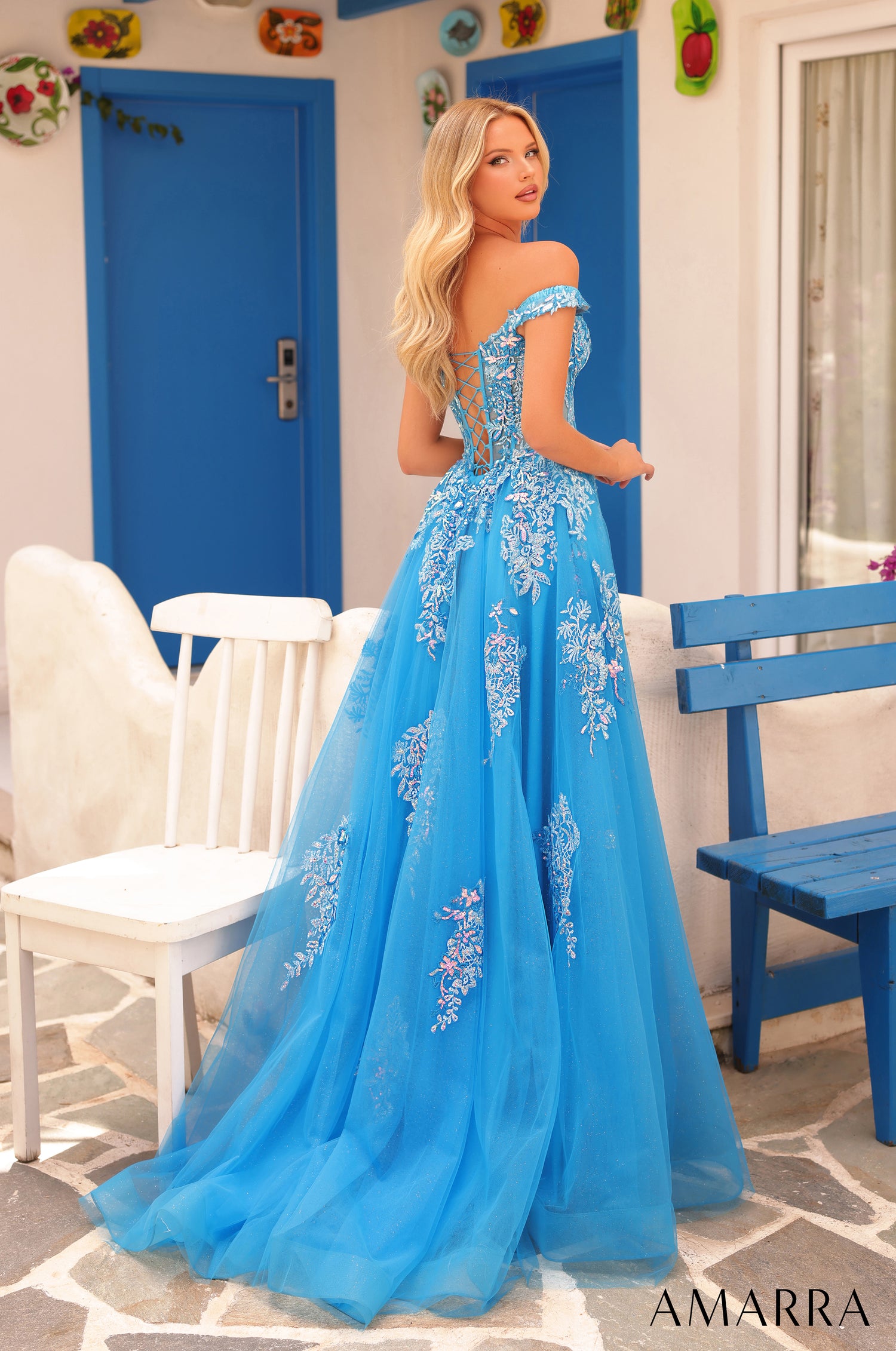 A woman wears a blue off-shoulder ball gown with floral embroidery.