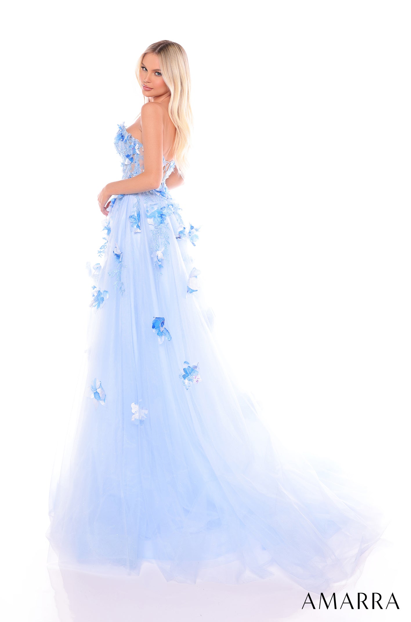 A blue tulle ball gown with 3D floral appliqués, worn by a blonde model against a white background.