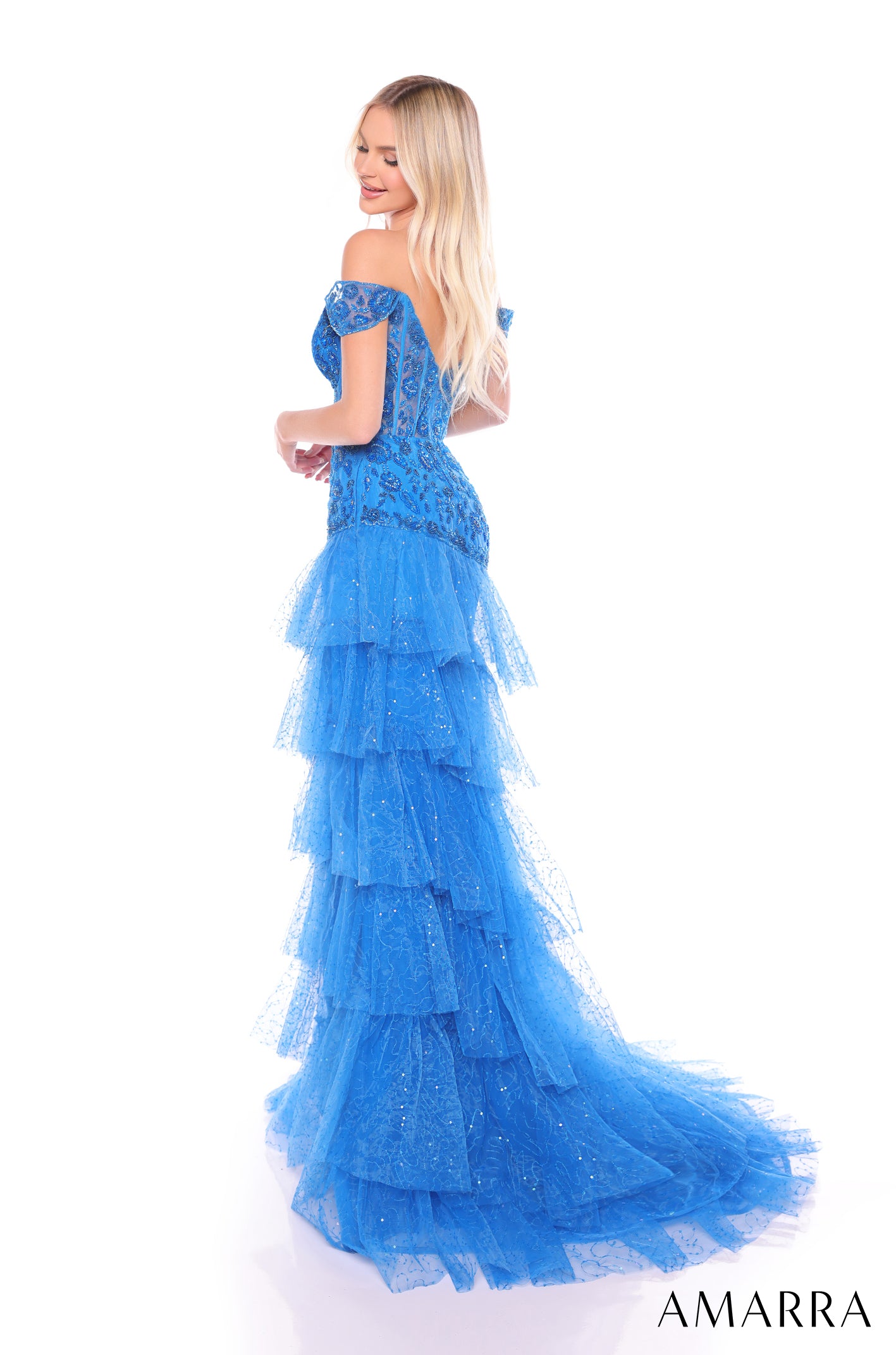 A blonde woman wears a blue off-shoulder tiered gown with sparkling tulle and a long train.