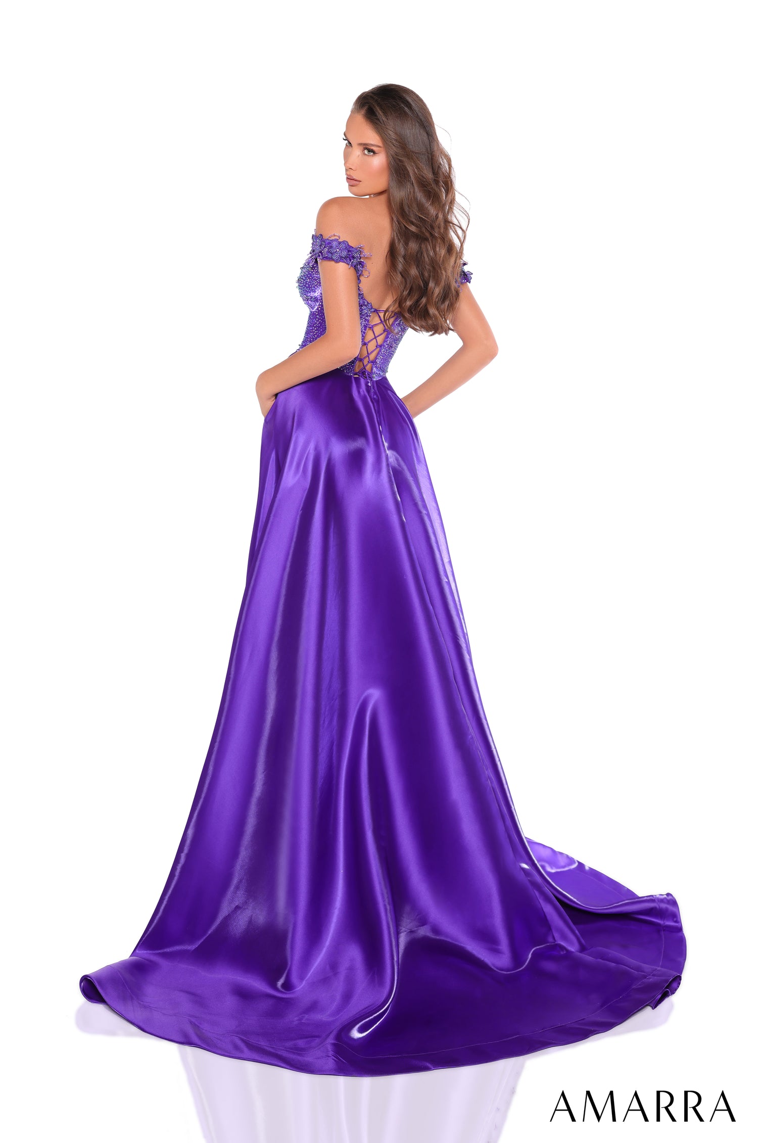 A woman wears a deep purple satin off-shoulder gown with a corset-style bodice and flowing train.