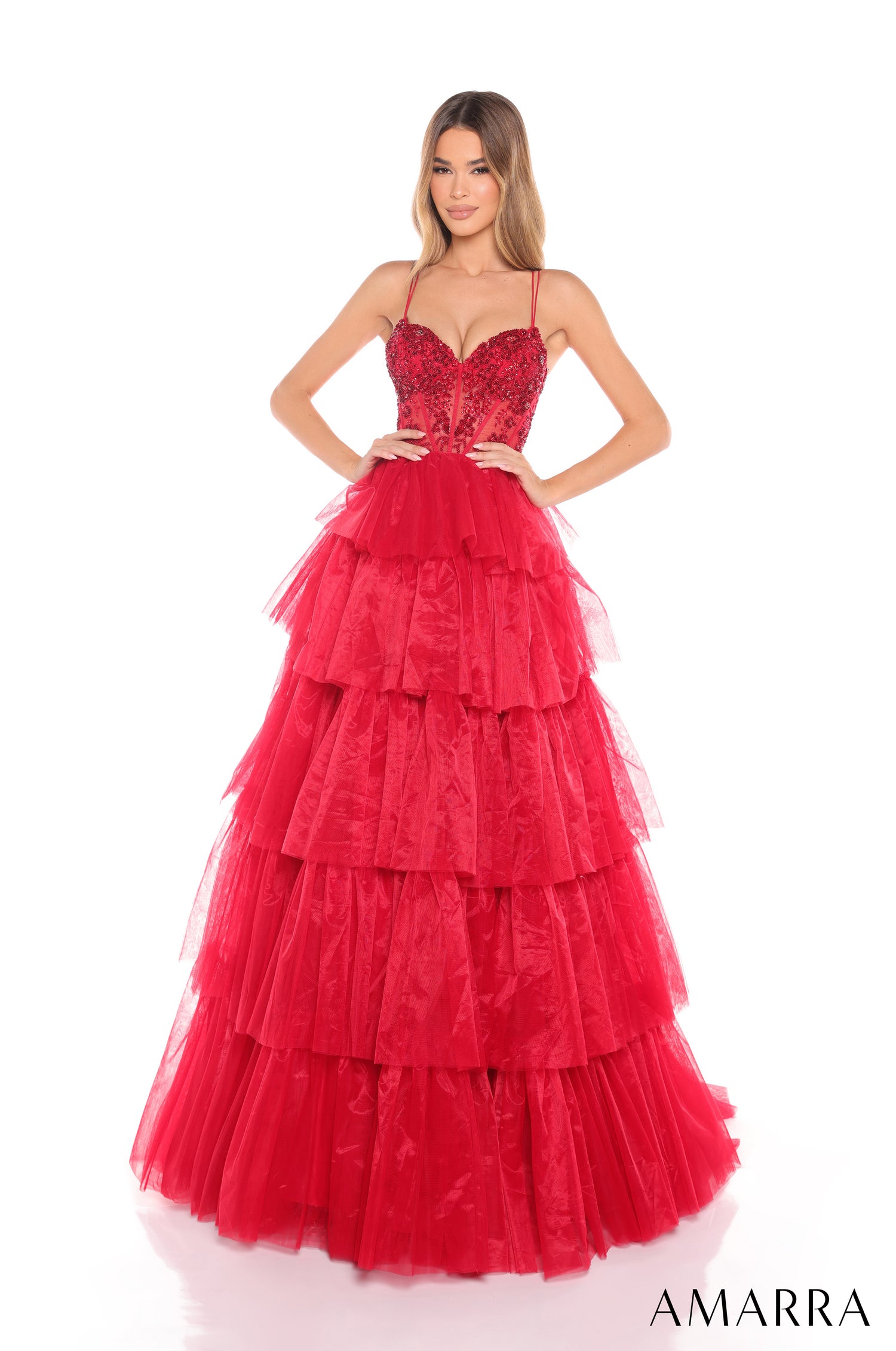 A woman wears a red tiered tulle ball gown with a beaded bustier bodice by Amarra.