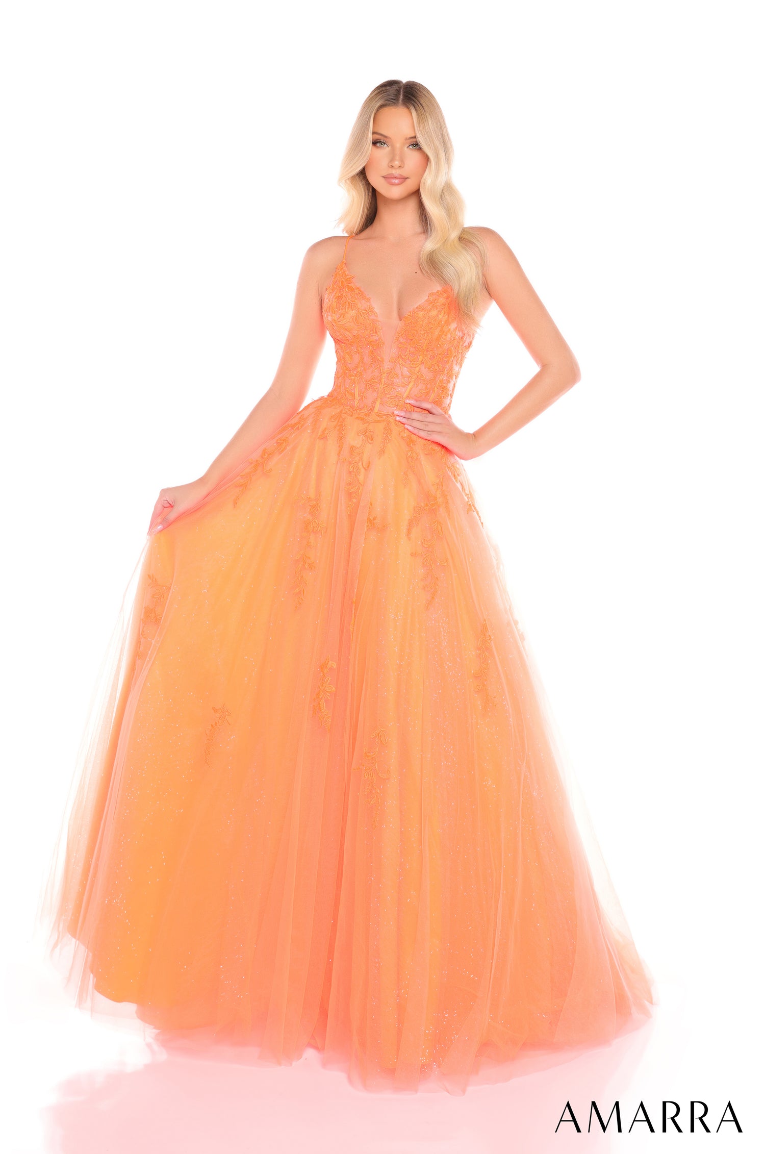 A blonde model wears a long, flowing Orange ball gown with a fitted bodice and tulle skirt by Amarra.