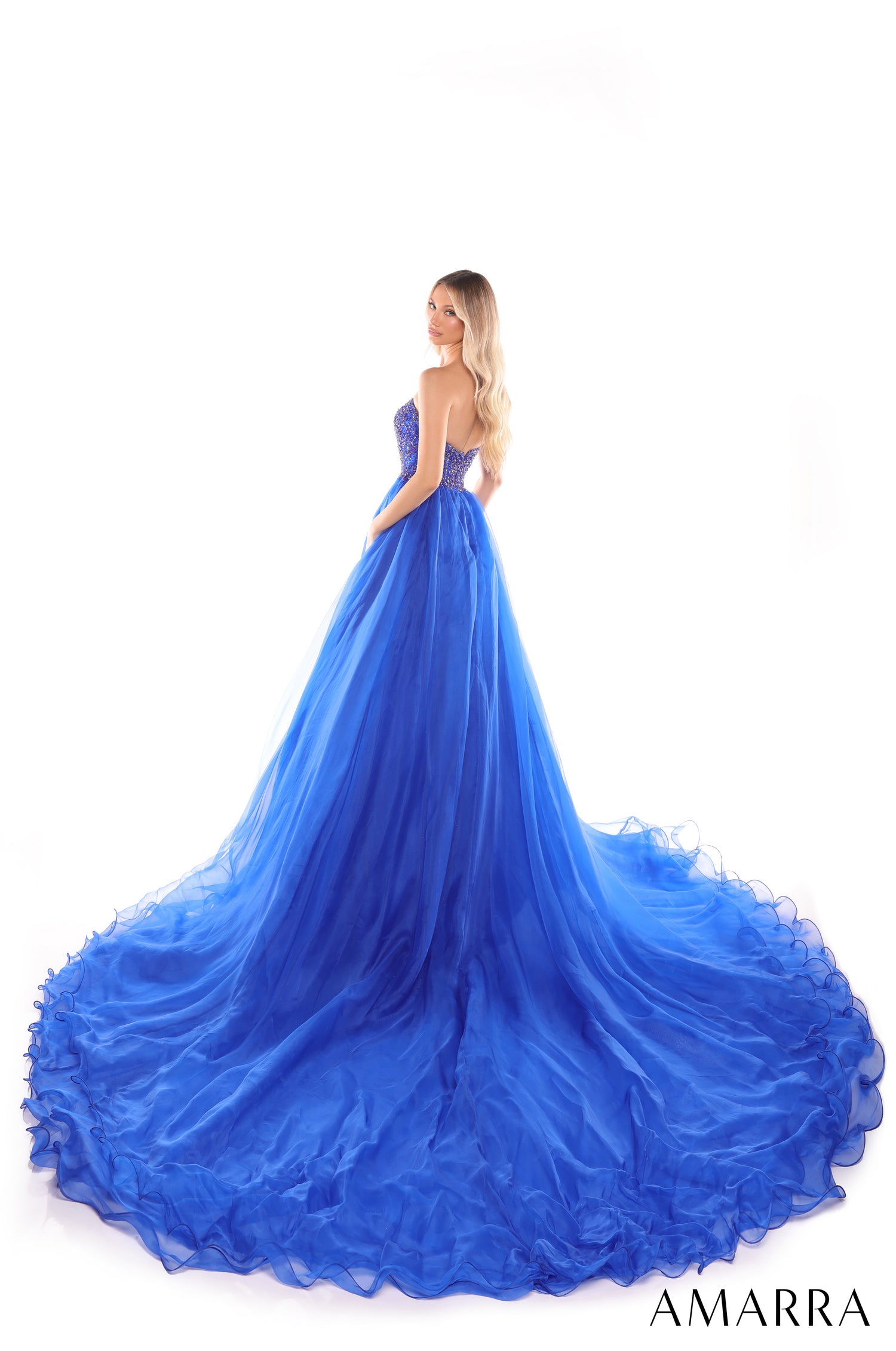 A woman wears a voluminous royal blue ballgown with a sweetheart bodice and dramatic ruffled train.