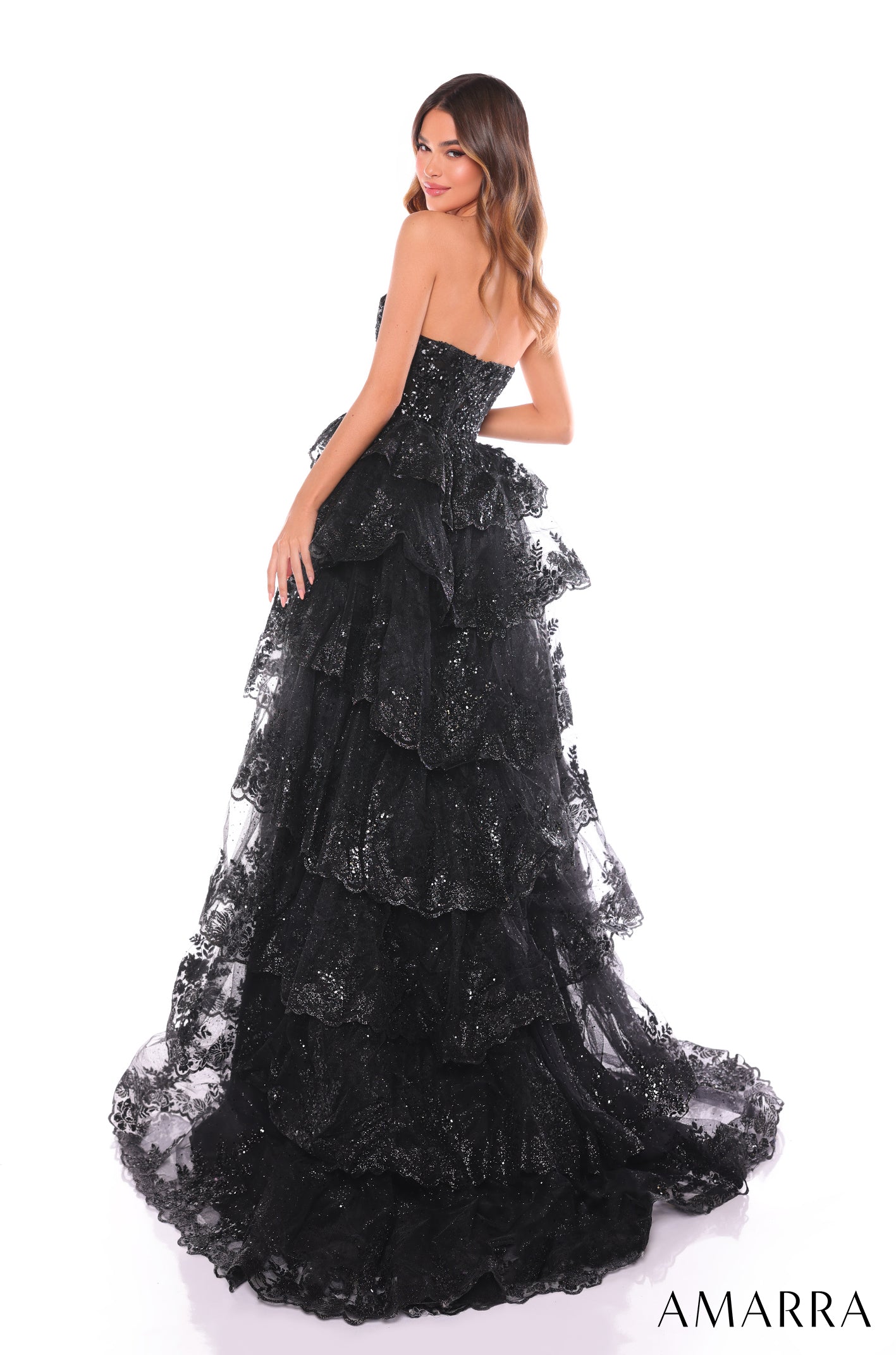 A strapless black sequined ball gown with tiered lace layers and a dramatic train, worn by a model.