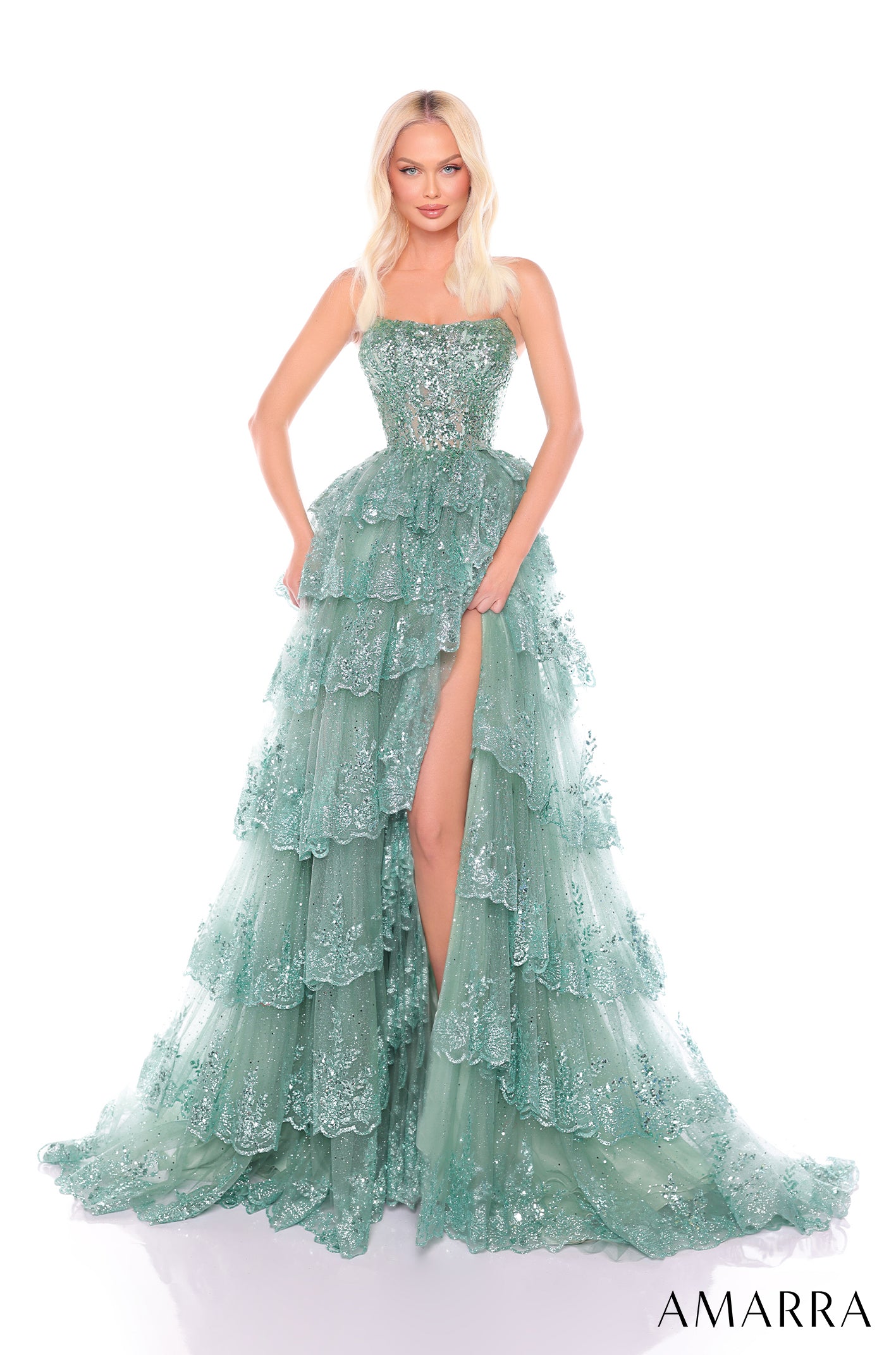 A model wears a sage green, multi-tiered ball gown with sparkling lace and a thigh-high slit.