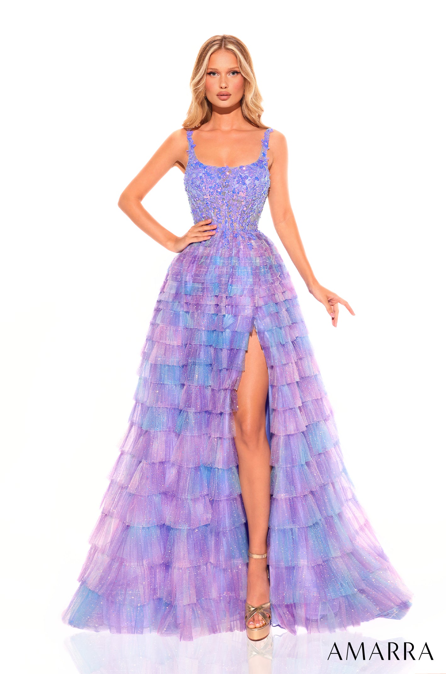 A tall model wears a tiered, shimmering Electric Blue ball gown with a thigh-high slit and fitted bodice.