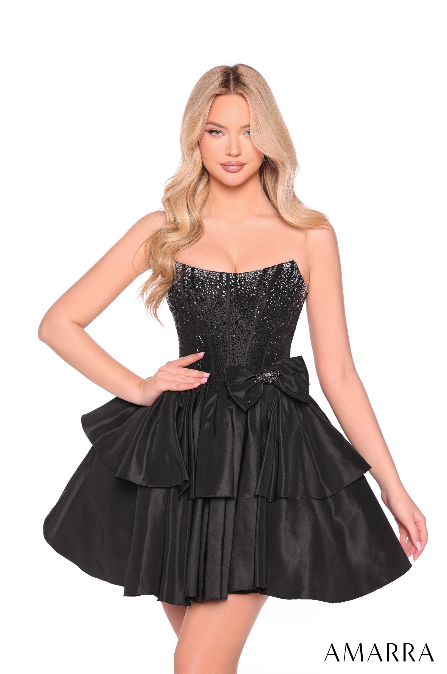 A blonde model wears a strapless, sequined Black cocktail dress with a tiered skirt and bow detail by Amarra.