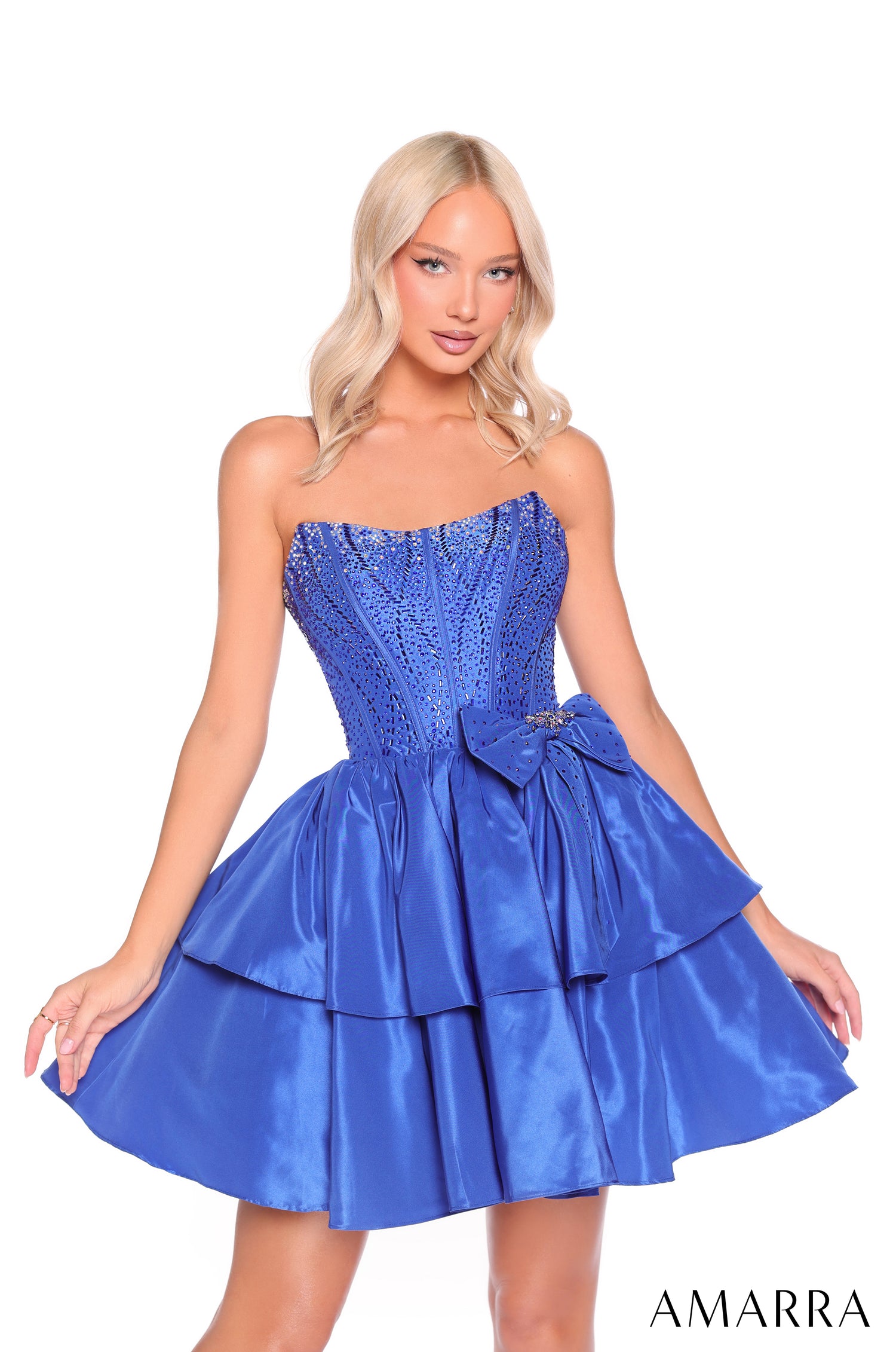 A blonde model wears a royal blue strapless cocktail dress with a sequined bodice and tiered skirt by Amarra.