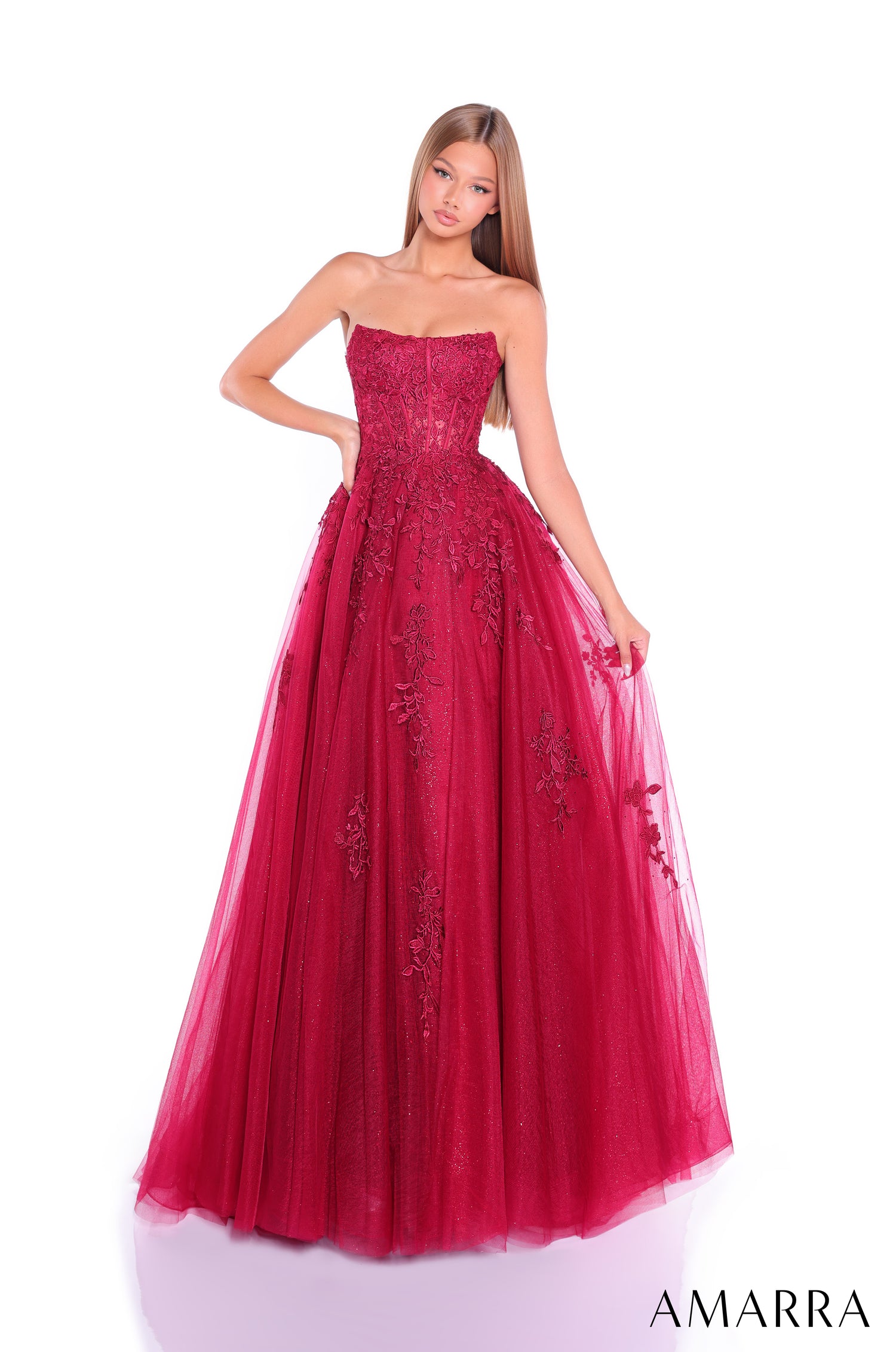 A model wears a strapless Wine-colored ball gown with floral lace embellishments and a full tulle skirt.