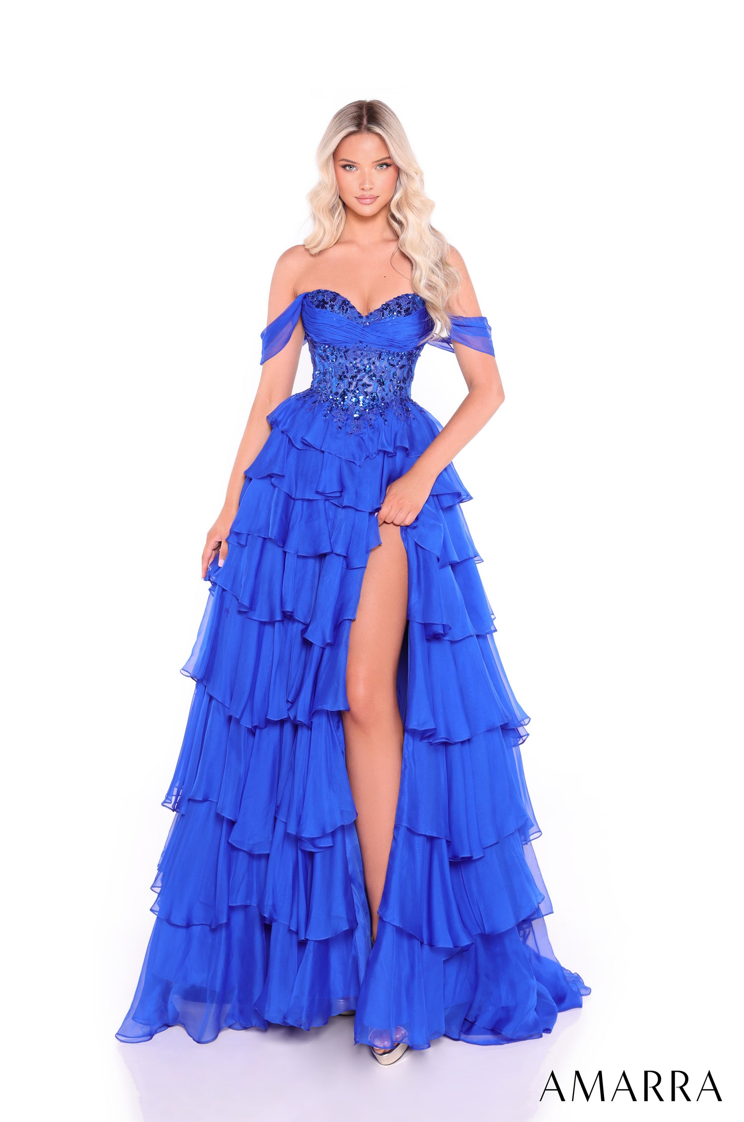 A woman wears a Royal Blue tiered gown with sequined bodice and dramatic off-shoulder design by Amarra.