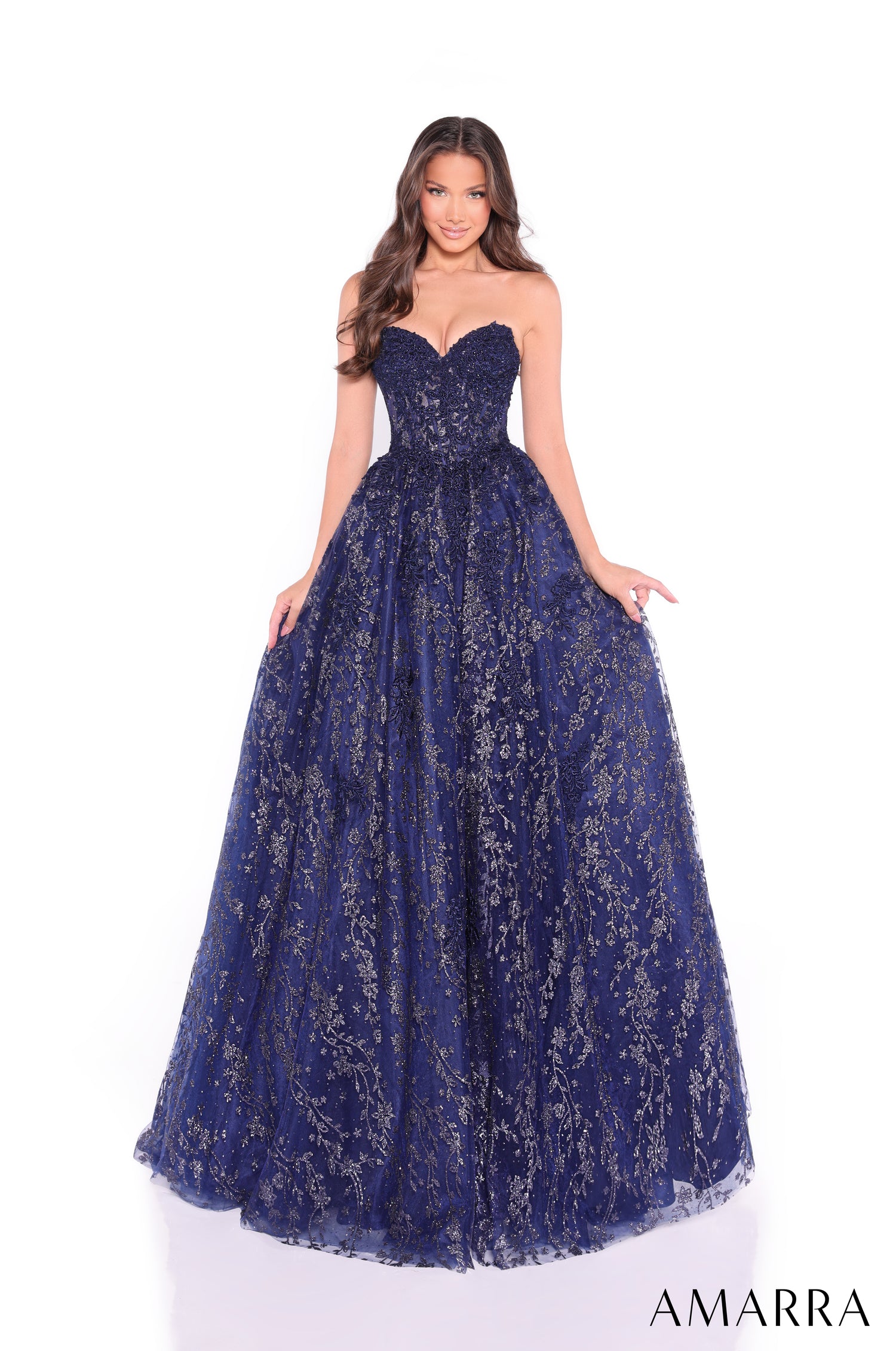 A woman wears a strapless navy ball gown with sparkling silver floral embellishments.
