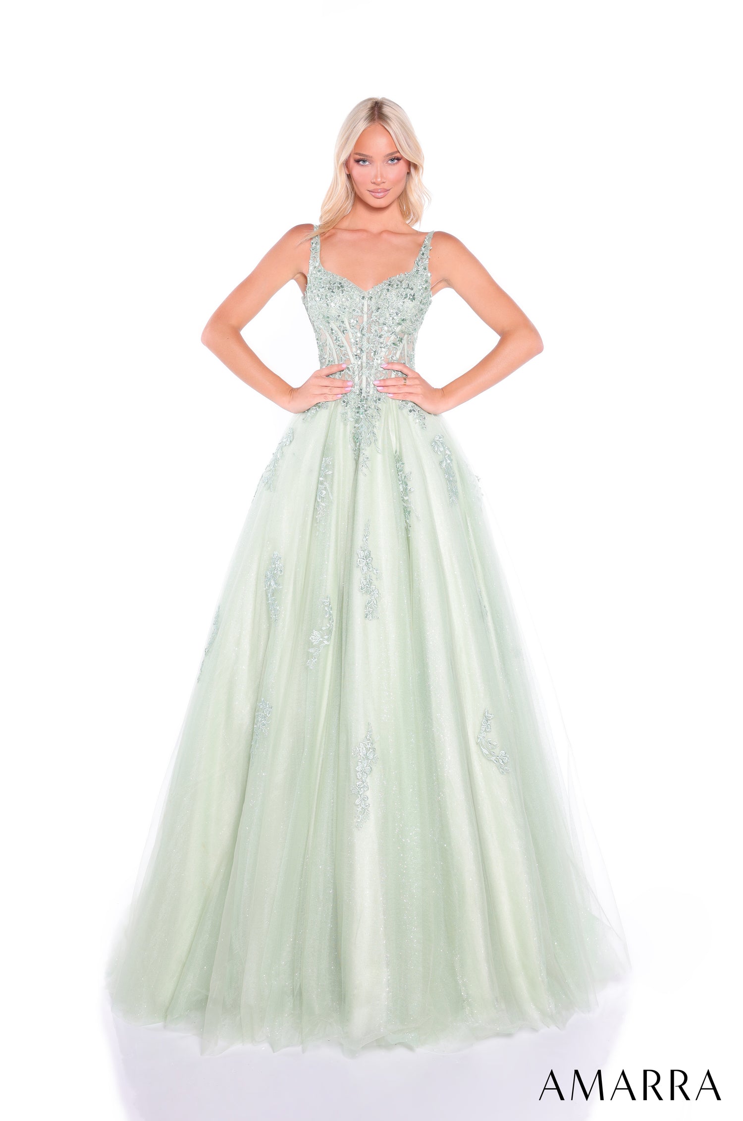 A woman wears a sage green ball gown with an embellished corset bodice and flowing tulle skirt by Amarra.