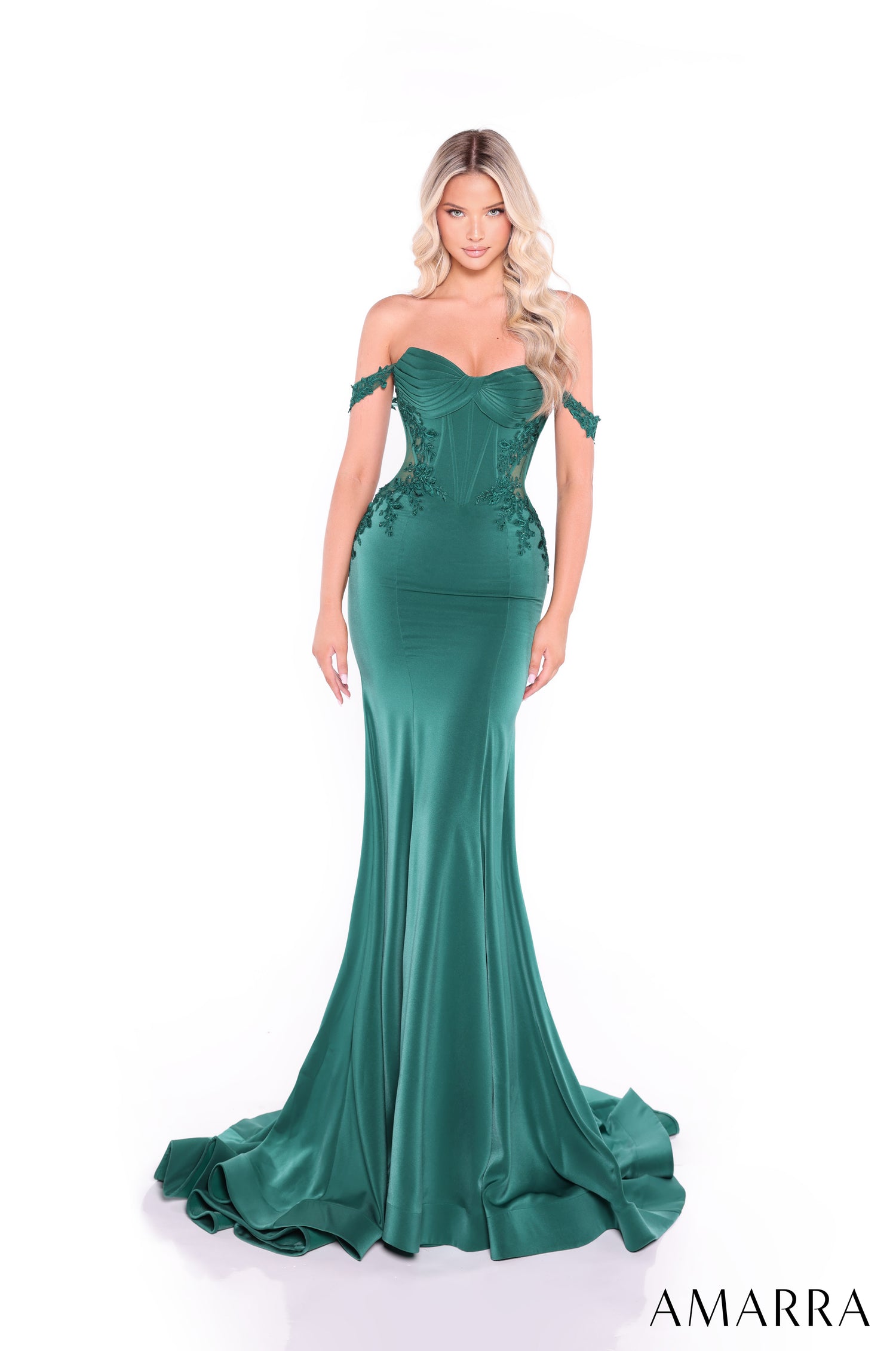 A model wears an emerald off-shoulder mermaid gown with lace details and a sweeping train.