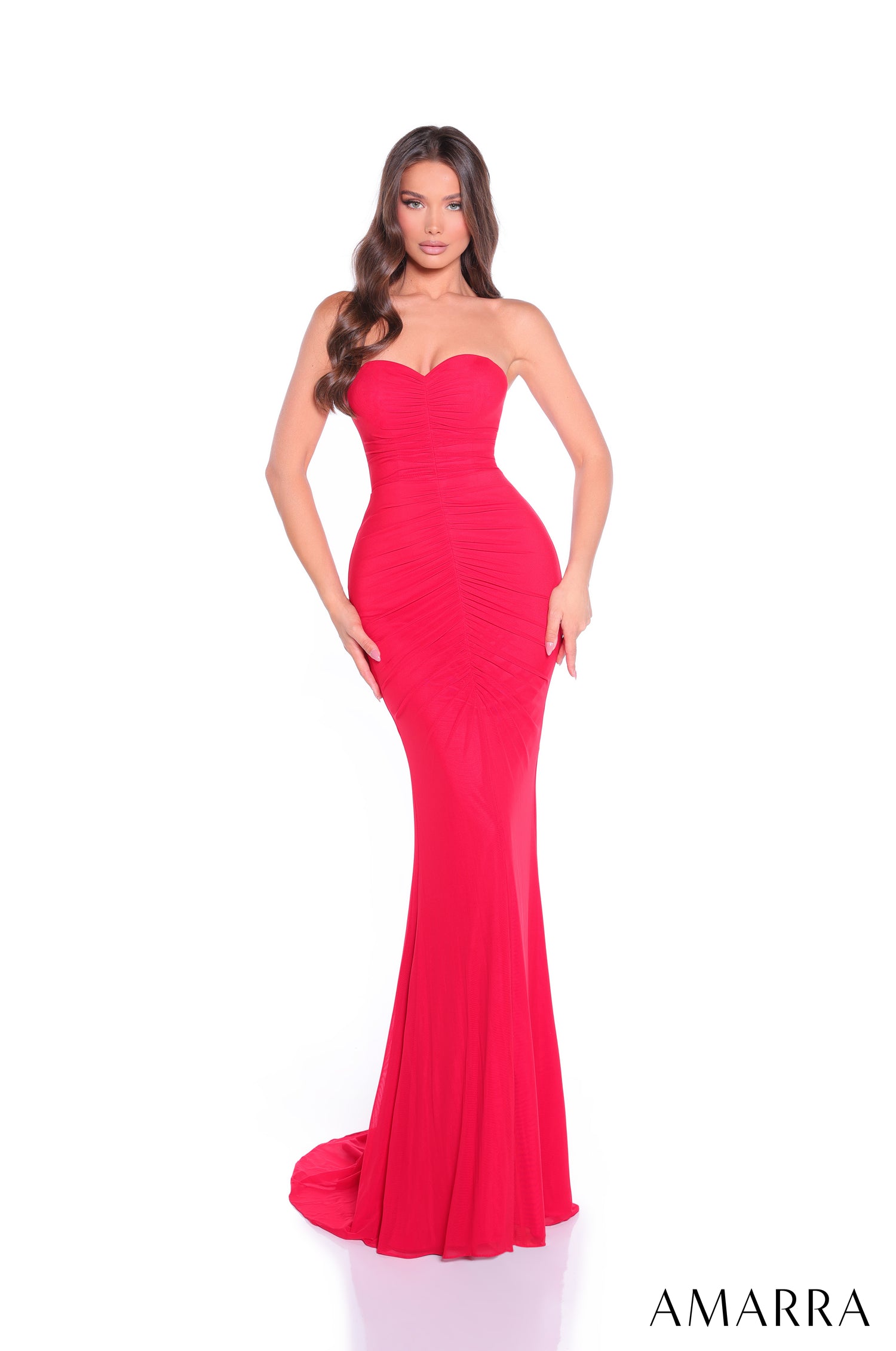 A woman stands wearing a strapless, form-fitting red evening gown with a sweetheart neckline and a long train.