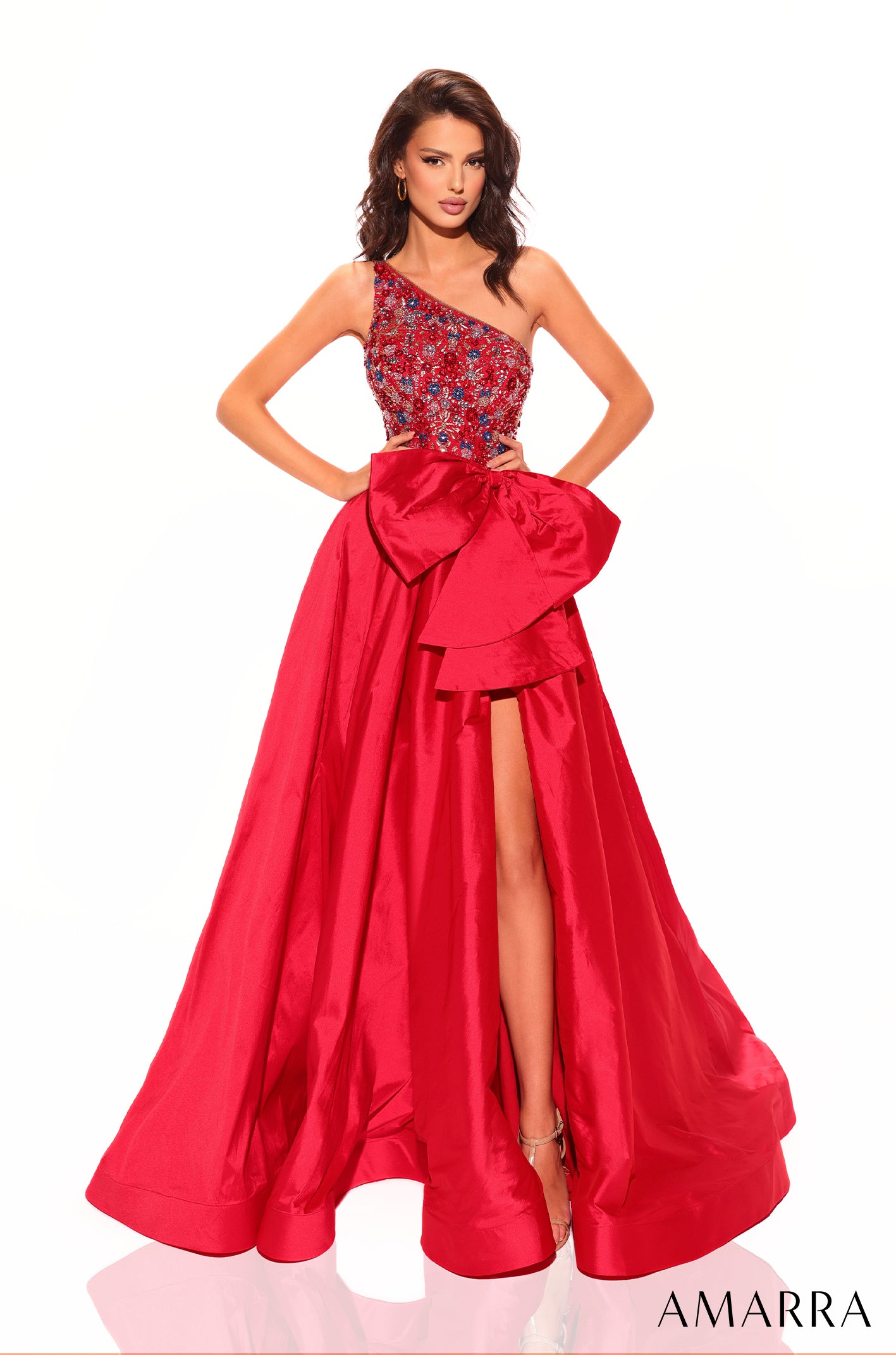 A model wears a one-shoulder Red ball gown with embellished bodice and dramatic bow, featuring a high leg slit.