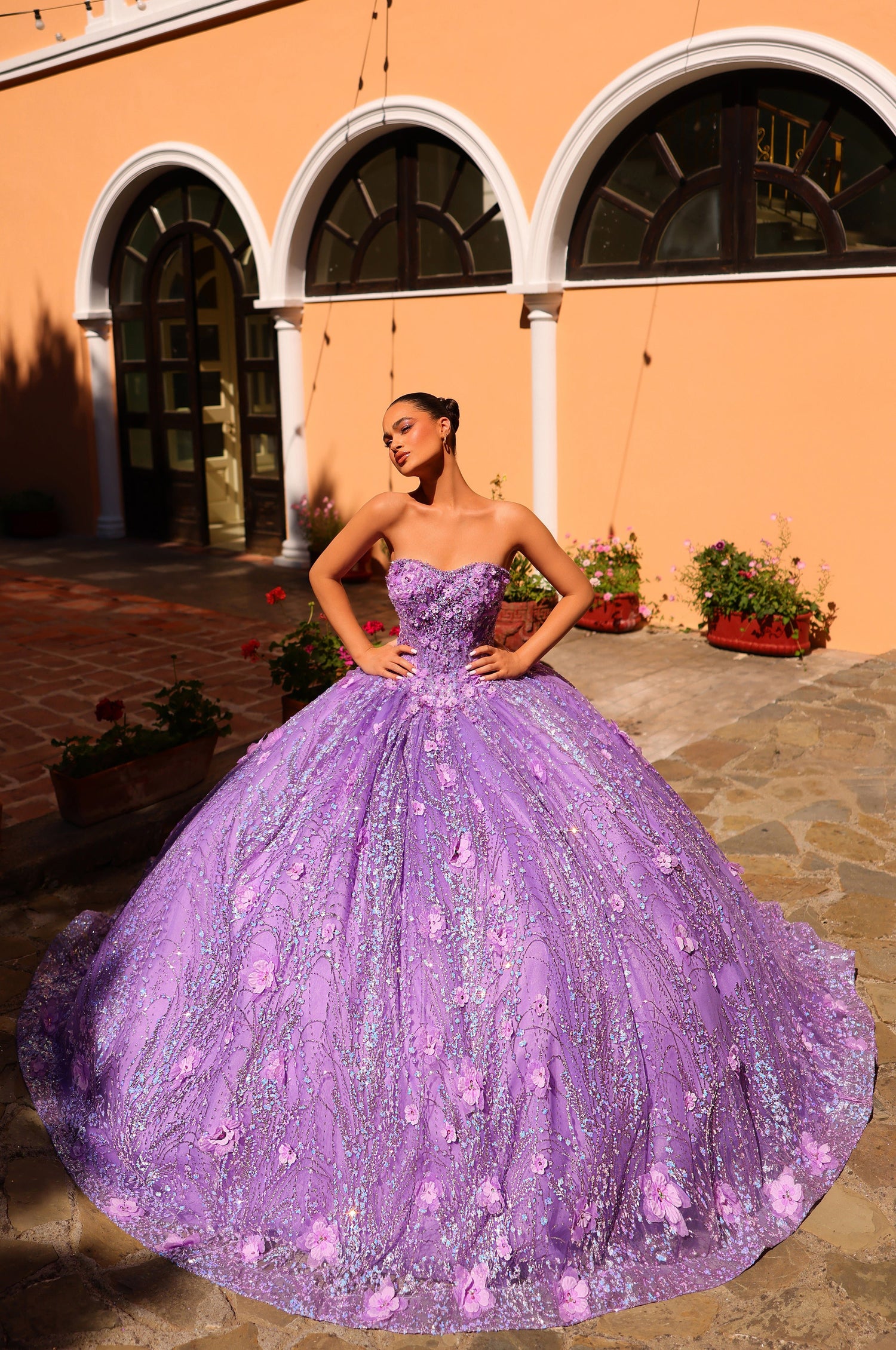 A woman in a lavender ball gown poses confidently before an arched architectural backdrop with flowers.