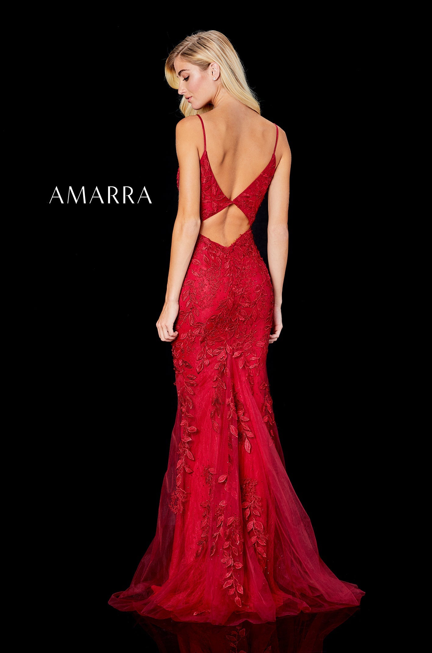 A red lace mermaid gown with a low back and train, modeled facing away on a black background.