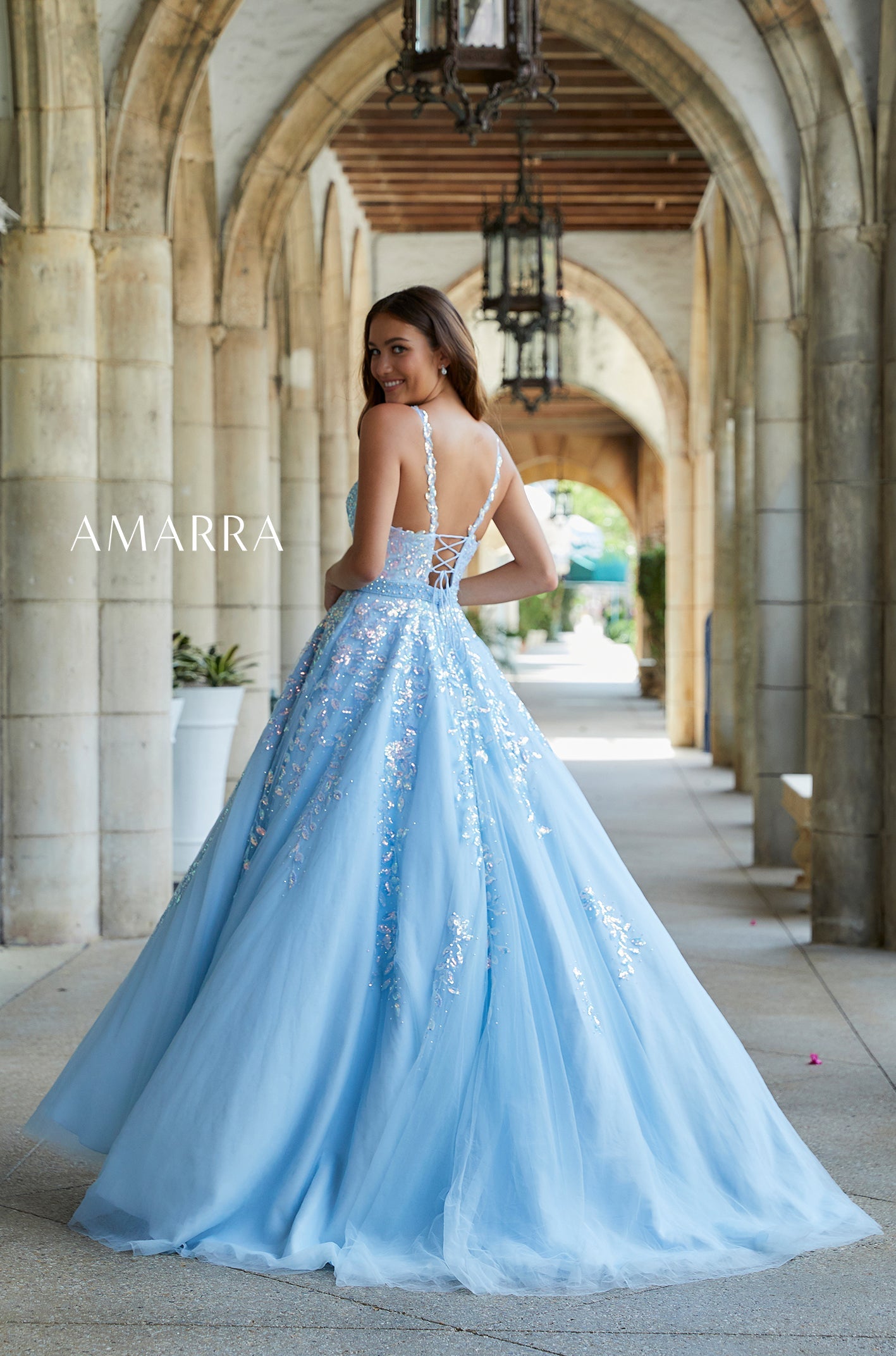 A light blue ballgown with sparkly embellishments, worn by a woman posing in an arched stone hallway.