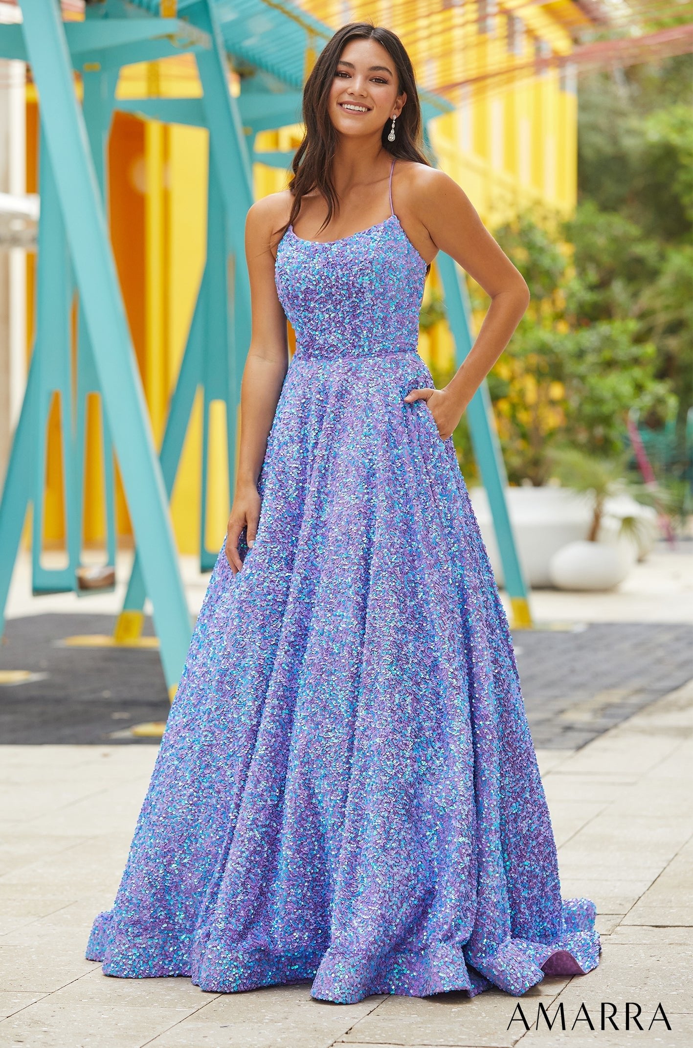 A woman in a sparkling blue and purple sequin ball gown stands confidently against a colorful background.