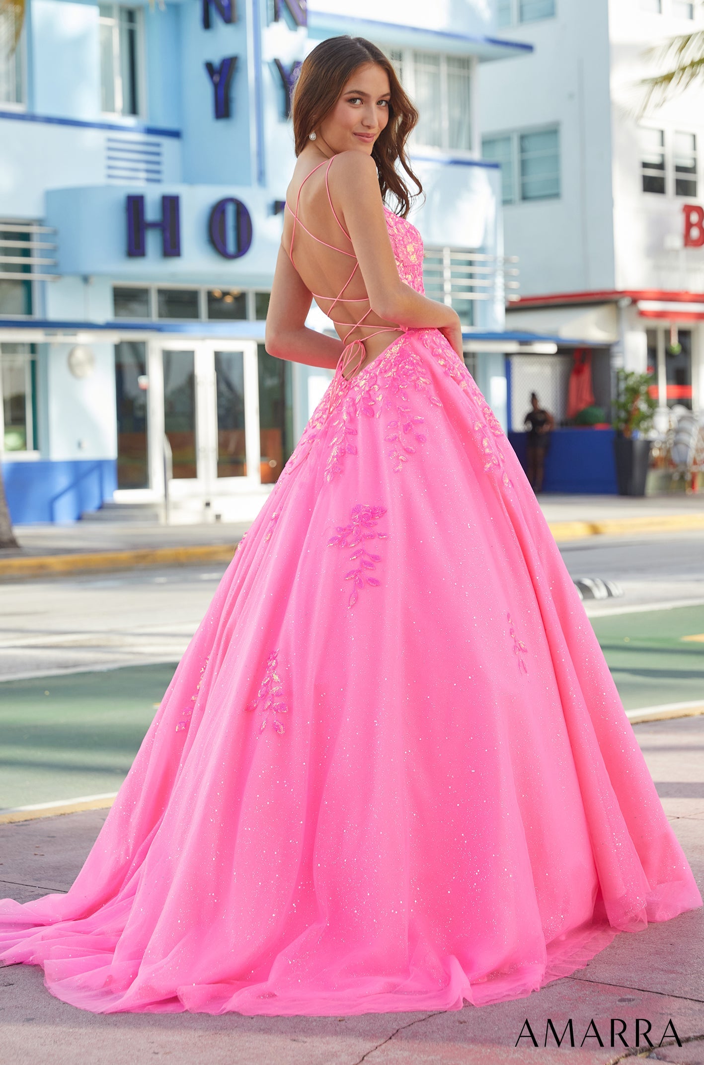 A vibrant pink ball gown with a lace-up back stands out against an urban backdrop.