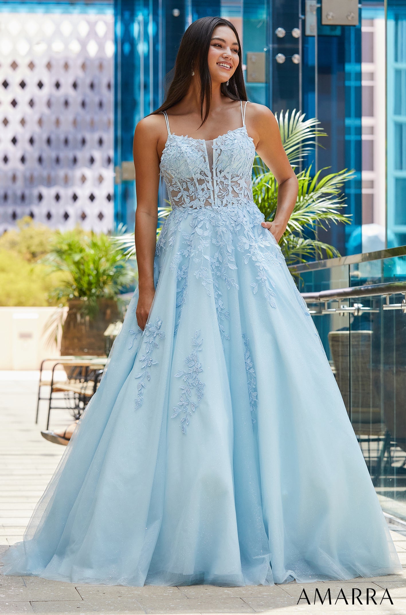 A light blue ball gown with floral lace details and a full tulle skirt, worn by a smiling woman.