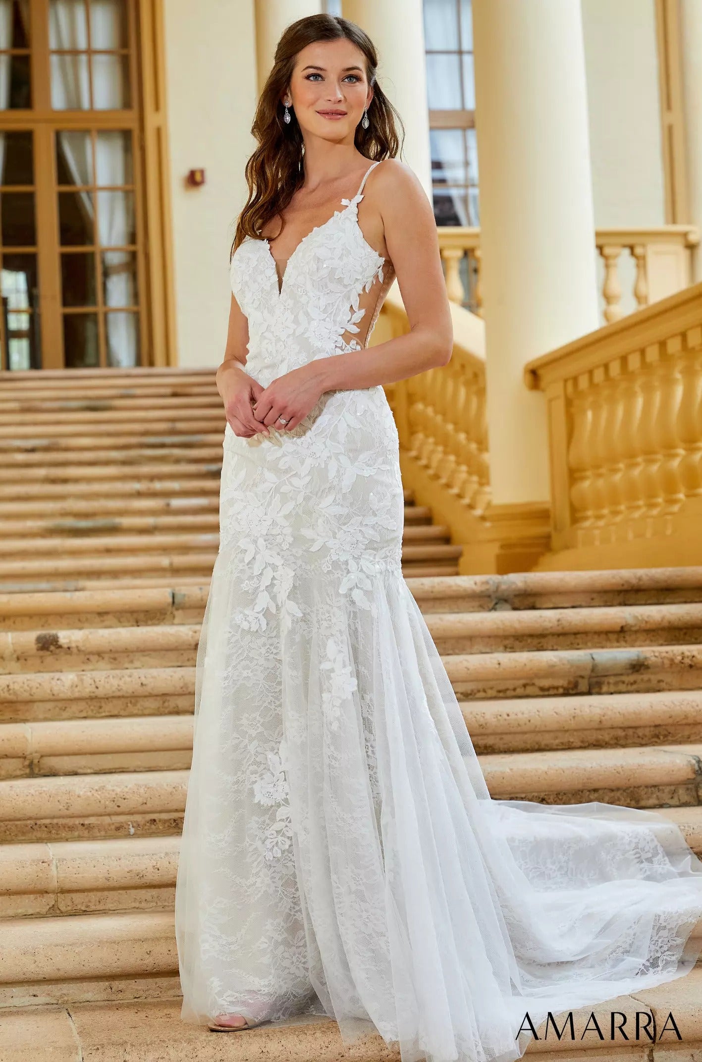 A white lace mermaid wedding dress with spaghetti straps and a long train, worn on stone steps.