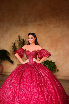 A woman in a vibrant red ball gown with sequined fabric and puffy sleeves poses elegantly against a warm background.