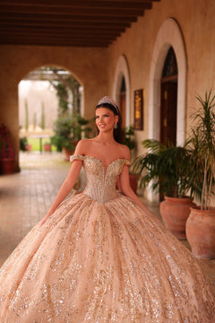 A glittering blush quinceañera ball gown with an off-shoulder bodice and sparkling embellishments in an arched courtyard.