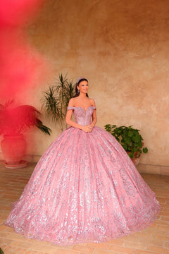 A woman in a rose gold sparkly ball gown poses in a sunlit room with potted plants.