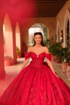 A woman in a vibrant red ball gown stands in an arched corridor with terracotta walls.
