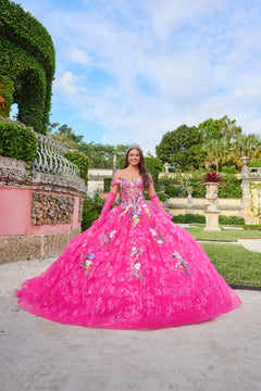 A young woman wears a voluminous Fuchsia/Multi floral quinceañera gown in an elegant garden setting.