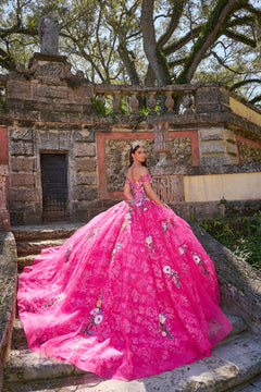 A woman in a vibrant pink floral quinceañera gown poses on stone steps with an ornate historic backdrop.