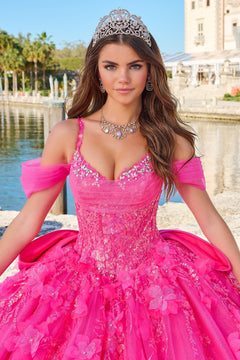 A woman in a vibrant pink quinceañera gown wears a sparkling tiara by a reflective water feature.