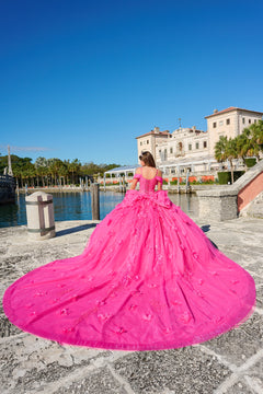 A person in a vibrant pink ballgown stands by a historic waterfront with an elegant building in the background.