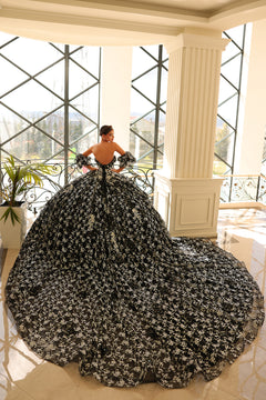 A woman wears a dramatic black and silver floral ball gown with a sweeping train in an elegant white-columned room.