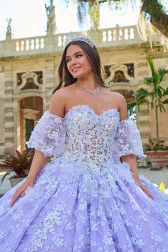 A young woman in a lavender quinceañera gown with floral lace and a tiara poses near a classical building.