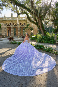 A lavender quinceañera gown spreads dramatically in a lush garden with an ornate historic building behind.