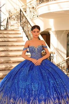 A woman in a royal blue, off-shoulder ball gown stands on an elegant staircase with ornate railings.